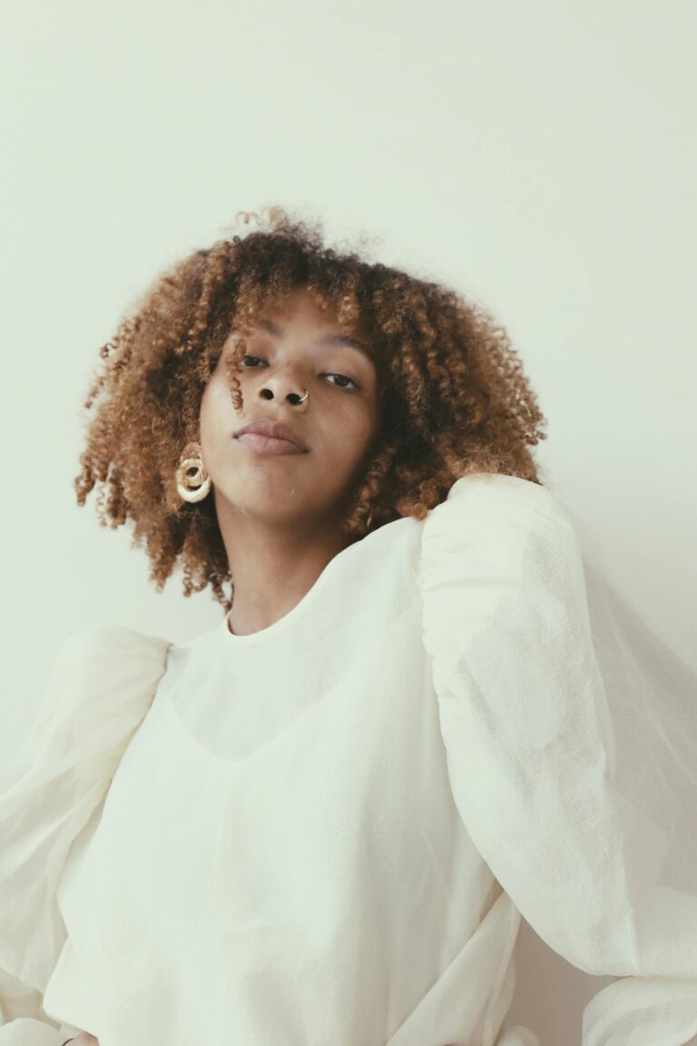 Stylish portrait of a black woman with curly hair and elegant white attire, embodying modern fashion.